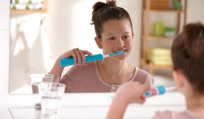 Cepillarse los dientes con un cepillo eléctrico para bebés.
