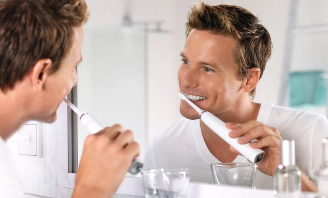 גבר מצחצח שיניים במברשת חשמלית